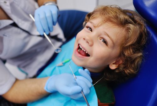 smiling child sitting in a blue chair dental